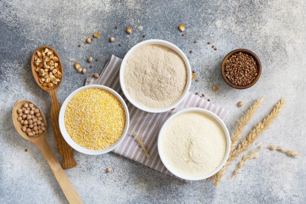 Cereals and flours coarse, corn flour, buckwheat flour, chickpeas flour over gray stone background.